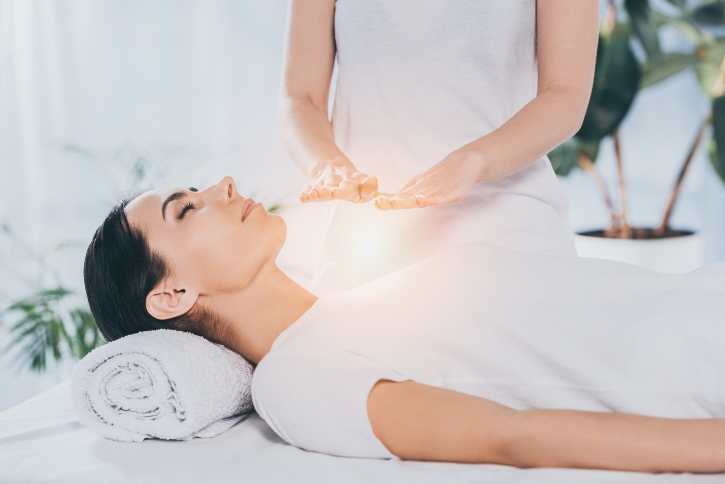 peaceful young woman with closed eyes receiving reiki healing treatment